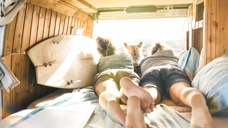 Hipster couple with cute dog traveling together on vintage van transport - Life inspiration concept with hippie people on minivan adventure trip watching sunset in relax moment - Warm sunshine filter