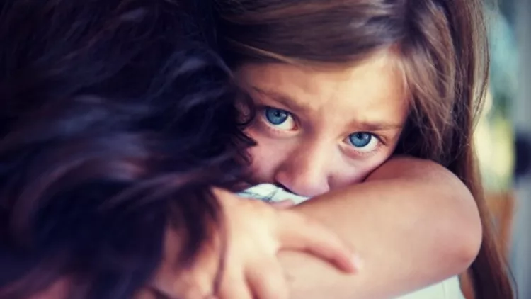 Closeup shot of a crying little girl hugging her mom around her neck