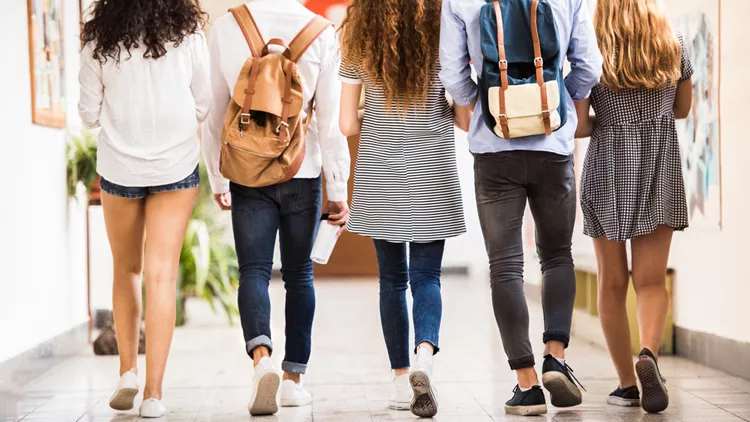 Unrecognizable teenage students in high school hall.