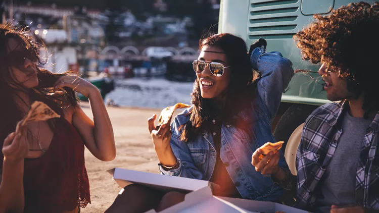 Friends eating pizza at the harbor close to vintage van