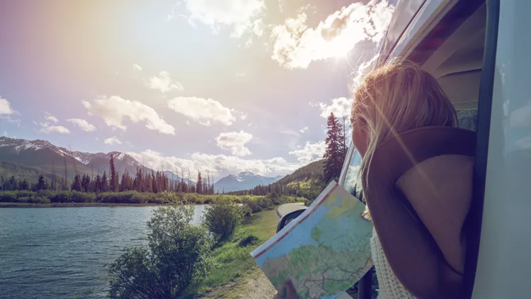 Young woman looks at road map near mountain lake