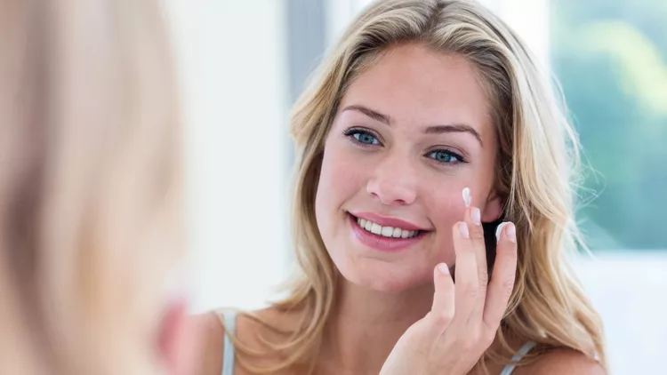 Smiling pretty woman applying cream on her face