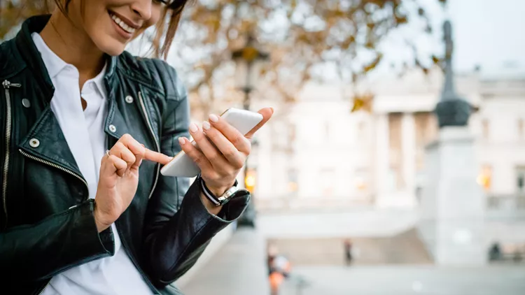 Happy woman using smart phone at Trafalgar Square in London, autumn season