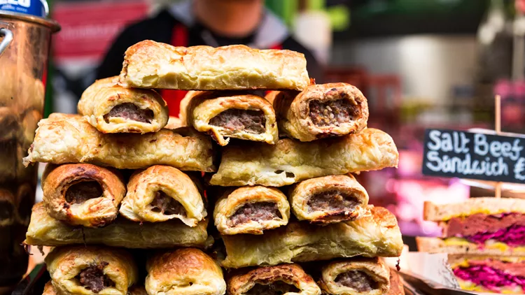 Close up of freshly cooked sausage rolls stacked in a row at food market