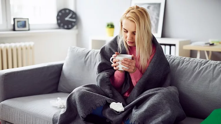 Young woman drinking tea while covered in blanket