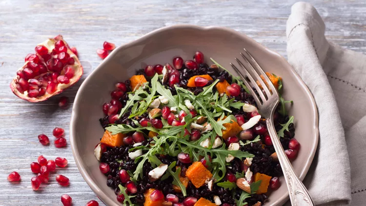 Salad with black rice, baked pumpkin, pomegranate seeds, arugula and nuts on a gray background