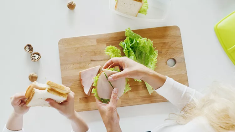 Mother with daughter eating sandwiches at home in the kitchen, top view