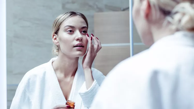 Blue-eyed woman putting some nourishing cream under her eyes