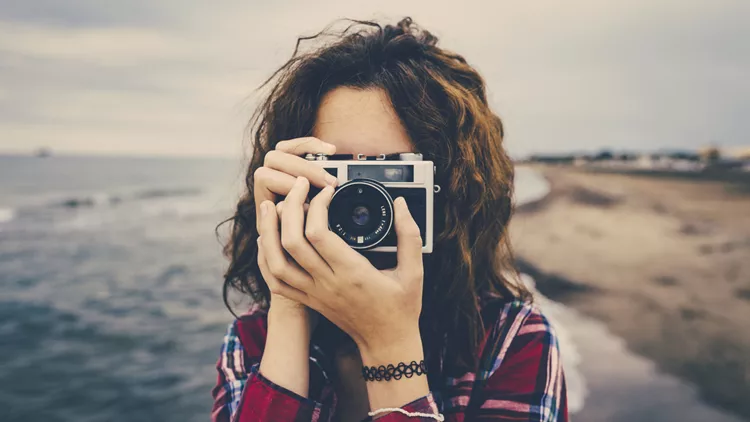 Girl taking a photo at sea with a film camera