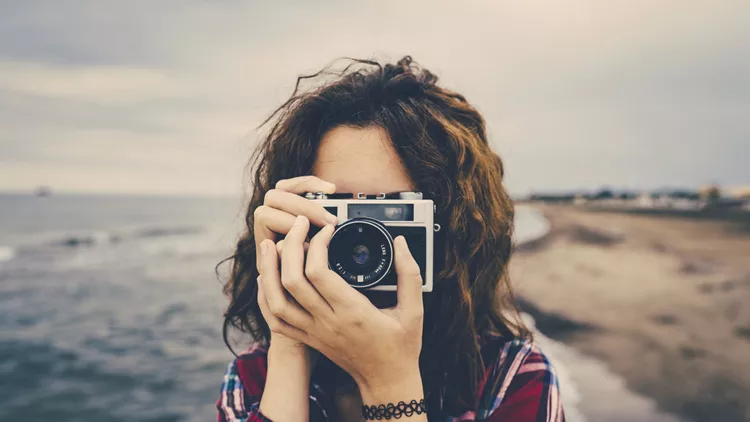 Girl taking a photo at sea with a film camera