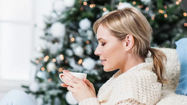 Young woman drinking tea by the Christmas tree