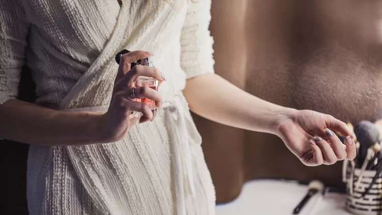 Beautiful young woman uses bottle of perfume at home, closeup