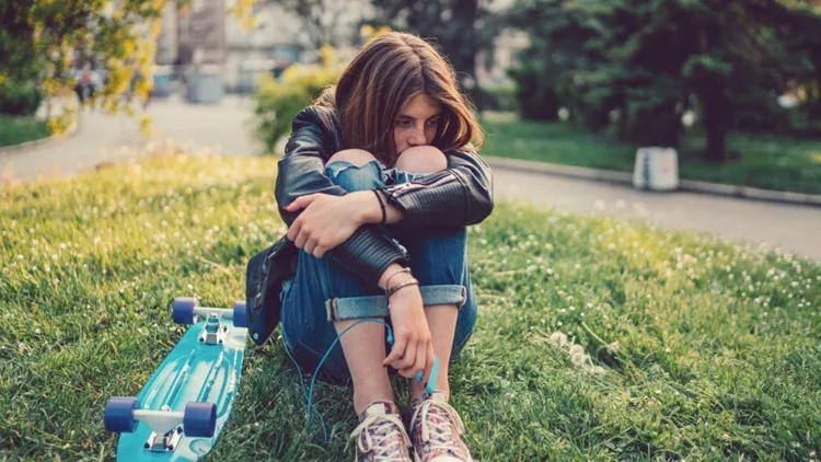 depressed-teenage-girl-with-skateboard-sitting-in-the-grass-picture-id959903202