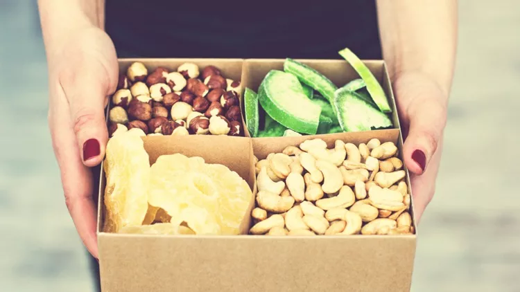 female-hands-hold-a-box-of-nuts-and-dried-fruits-picture-id941523544