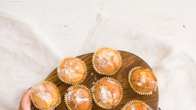 Top view on woman's hands holding wooden board with freshly baked home muffins on white table background.