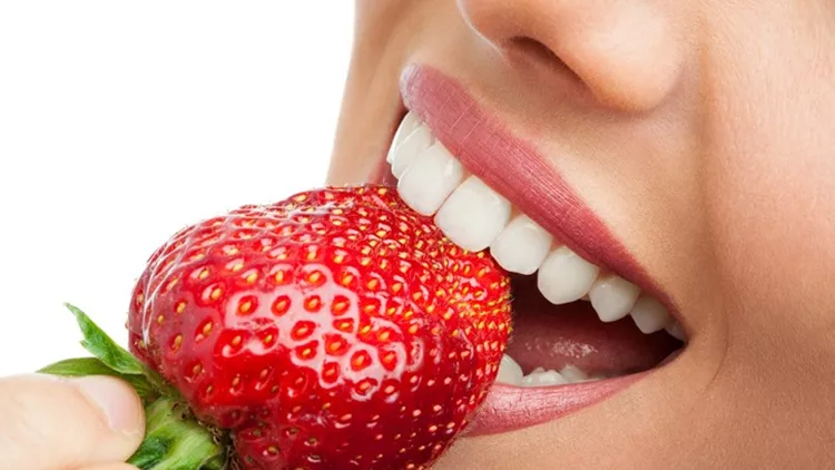 Extreme close up of teeth biting strawberry.