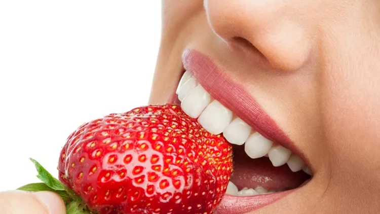 Extreme close up of teeth biting strawberry.