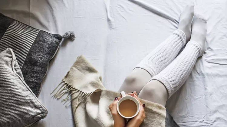 young woman on a bad holding a cup of coffee