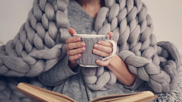 Cozy Woman covered with warm soft merino wool blanket reading a book. Relax, comfort lifestyle.