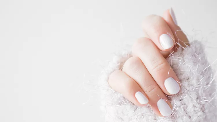 Beautiful groomed woman's hands with white nails on the light gray background. Nail varnishing in white color. Manicure, pedicure beauty salon concept. Empty place for text or logo.