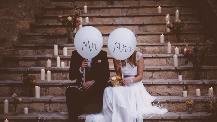 Newlywed couple sitting on steps and holding balloons