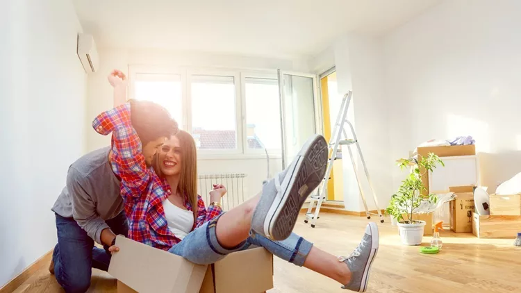 Happy young couple just moved new home unpacking boxes; having fun