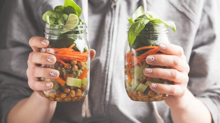 woman-holds-and-eats-a-salad-in-a-glass-jar-with-baked-chickpeas-and-picture-id918079594