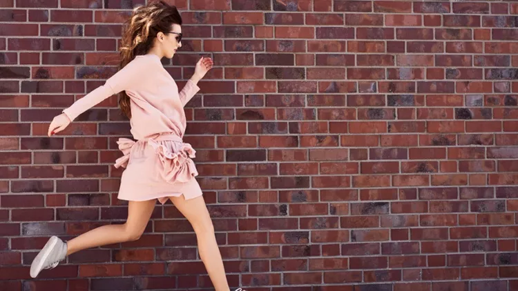 young-woman-jumping-on-city-street-with-brick-wall-in-background-picture-id888772240