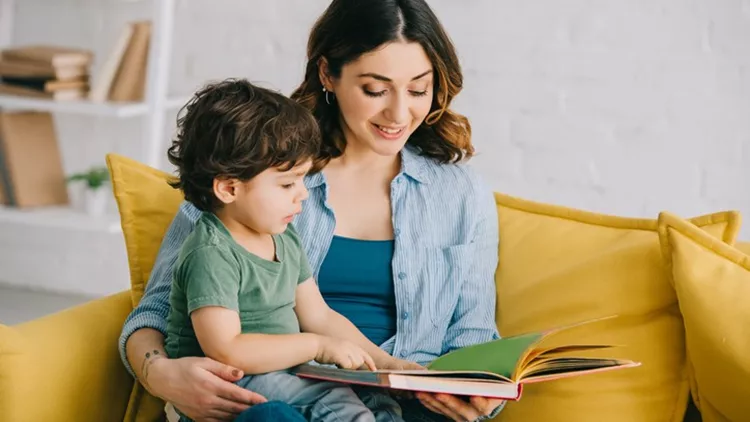 Mom and son sitting on yellow sofa and reading book