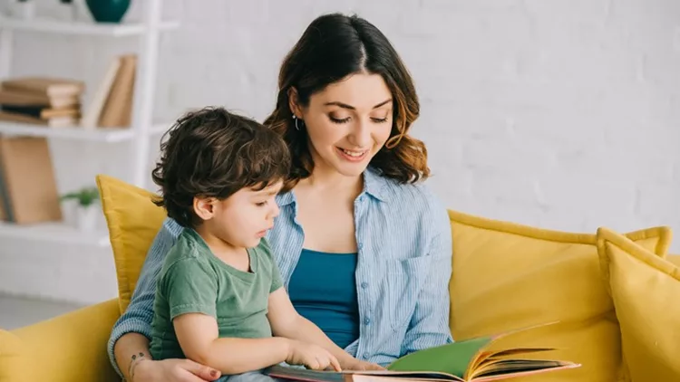Mom and son sitting on yellow sofa and reading book