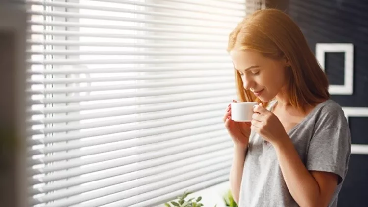 Happy young woman meets   morning with  cup of coffee  at   window