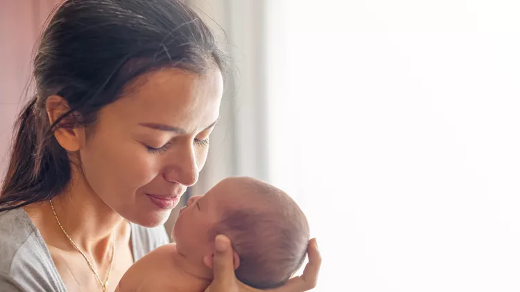 Beautiful mother kissing here little cute baby on her palm. Mother take care her little girl at home. One week newborn girl.