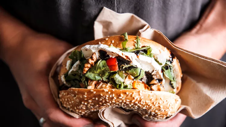 Woman is  holding a bagel fresh burger before eating.