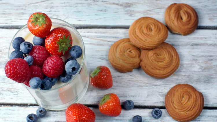 Panakota with berries in a glass, biscuits lying on a wooden table, top view, layout.