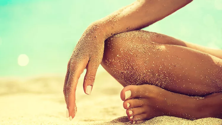 Womans hand is laying on the covered by sea sand knee.