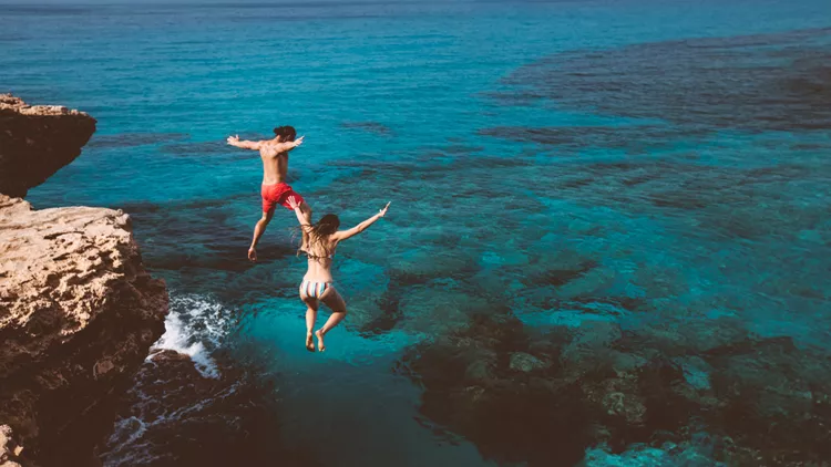 Young brave divers couple jumping off cliff into ocean