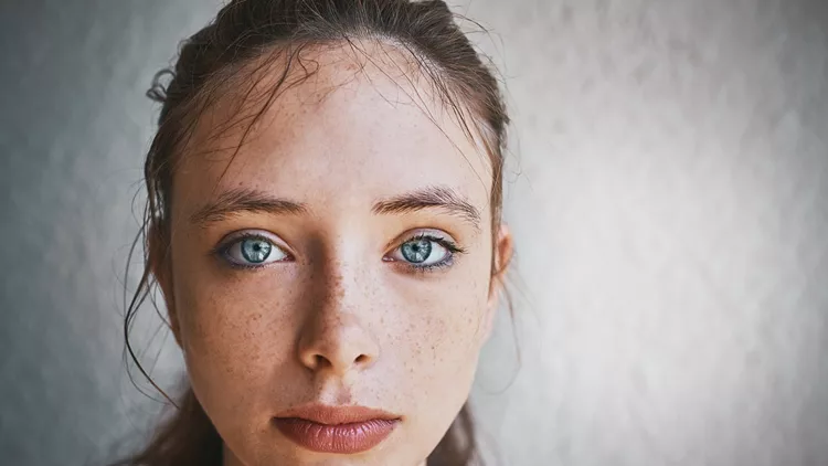 Beautiful blue-eyed brunette standing by textured wall looks sad