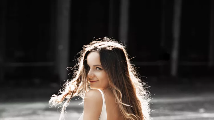 Portrait of a amazing caucasian bride with long hair looking sensual over the shoulder at the camera against sunrise.