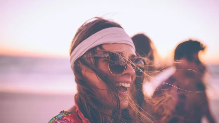 Boho Girl in sunglasses laughing on a beach with friends