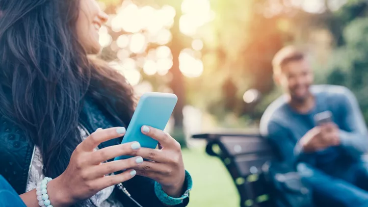 Flirting couple in the park texting on smartphones