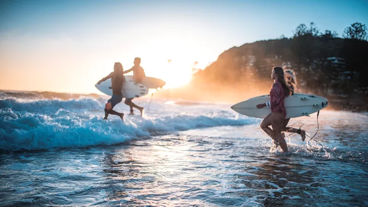 Friends running into the ocean with their surfboards