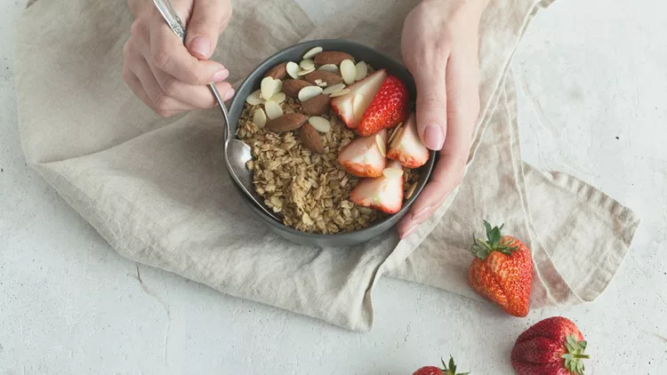 Healthy breakfast. Grey ceramic bowl with granola, strawberry and nuts in woman's hands. Diet and vegetarian food concept