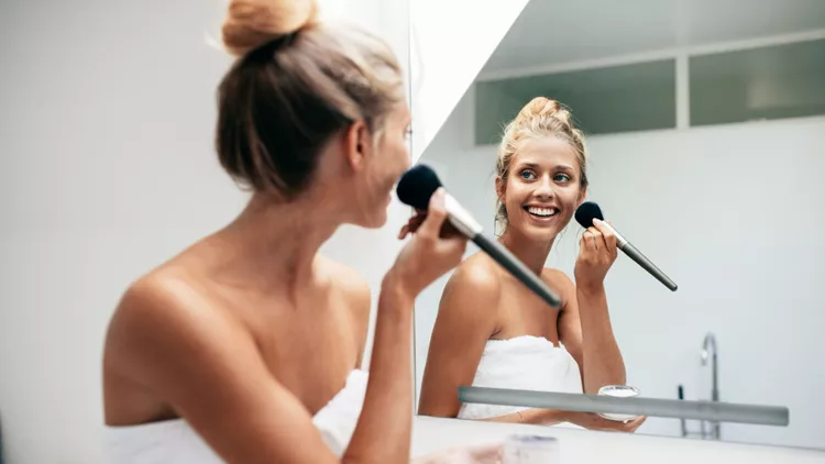 Beautiful young woman applying makeup in bathroom