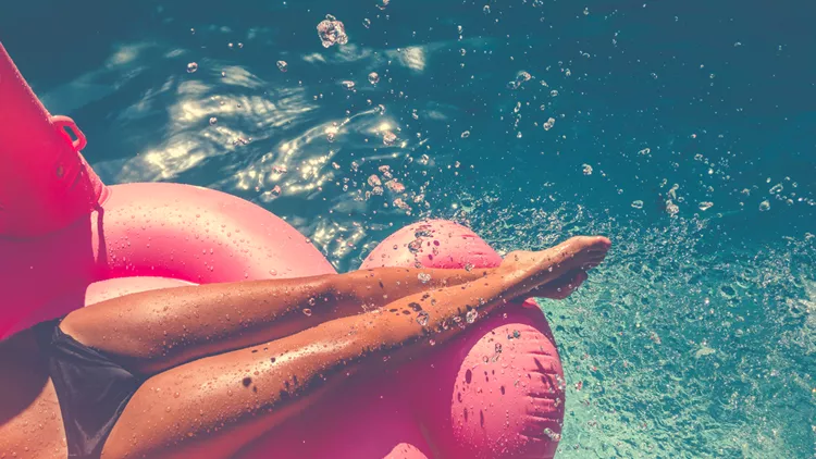 Woman floating on a pink inflatable in swimming pool.