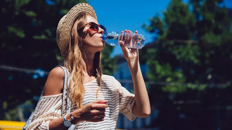 Trendy woman drinking a water from bottle, outdoors.