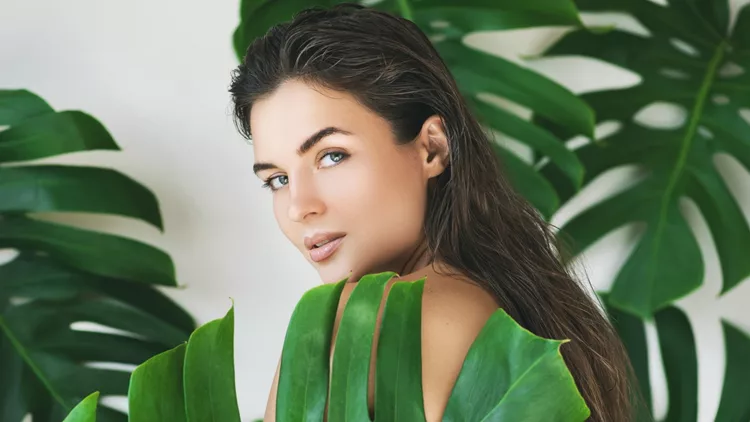 Portrait of young and beautiful woman with perfect smooth skin in tropical leaves