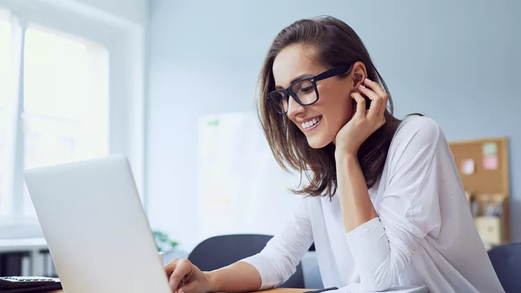 Portrait of beautiful cheerful young businesswoman working on laptop and laughing in home office