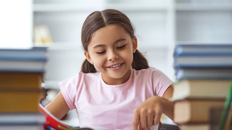 The happy schoolgirl sitting at the desk with books