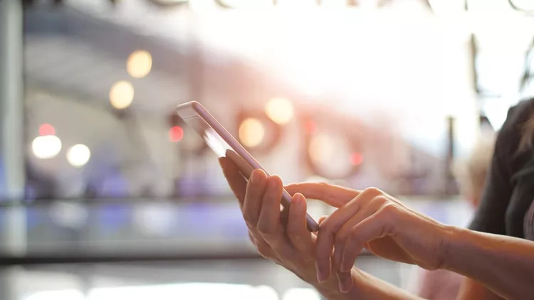 Close up of women's hands holding smartphone. Her watching sms, message, e-mail on mobile phone in coffee shop. Blurred background.