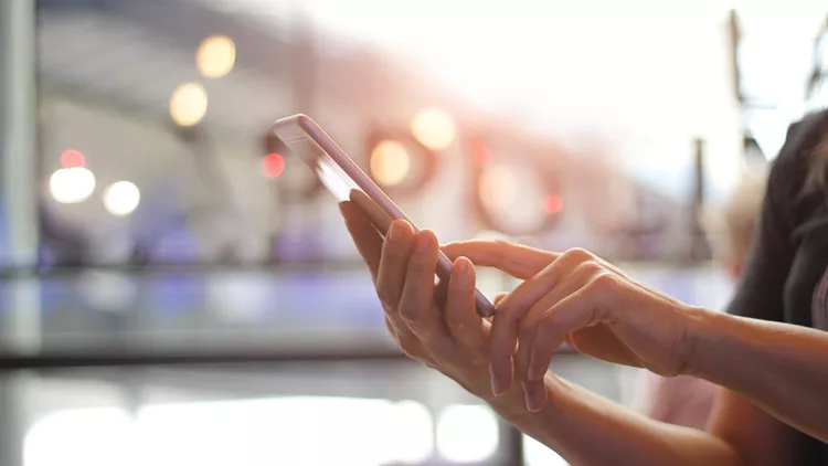 Close up of women's hands holding smartphone. Her watching sms, message, e-mail on mobile phone in coffee shop. Blurred background.